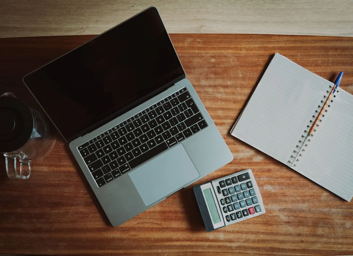Schreibtisch mit Laptop, Taschenrechner und Notizen zur Lohnabrechnung